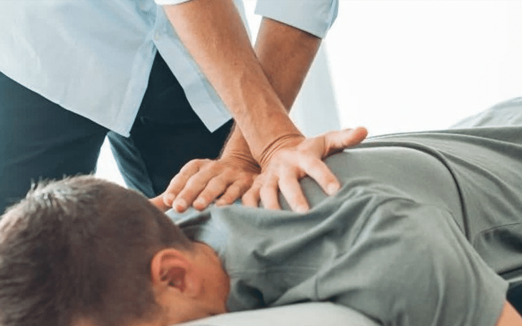 Male laying face down on a chiropractor's table with a Chiropractors hands on his upper back